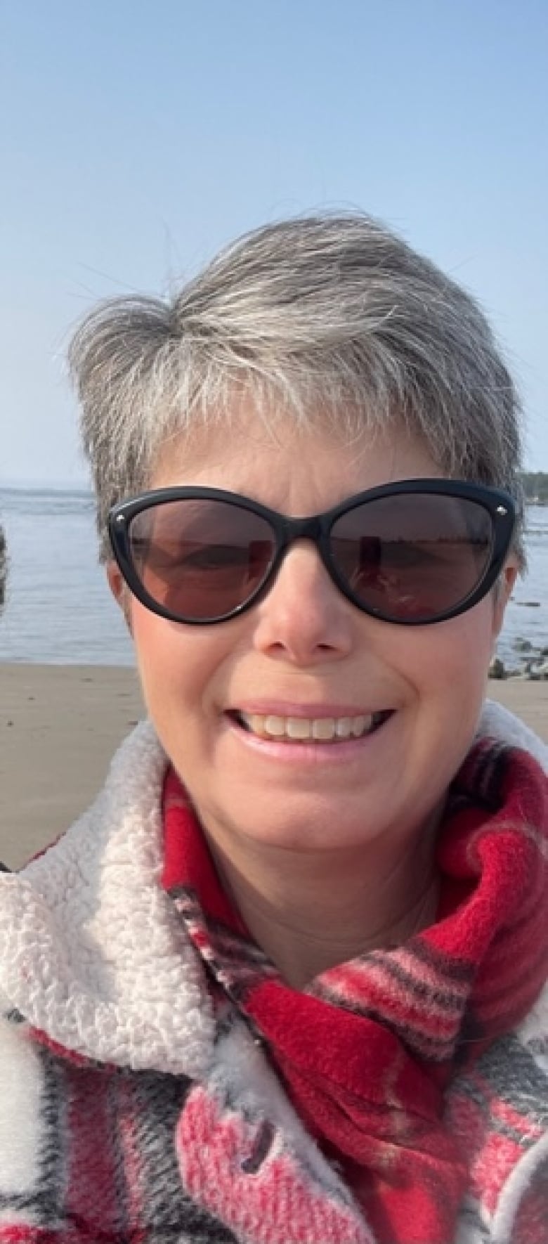 A woman with grey hair and sunglasses smiles at the camera